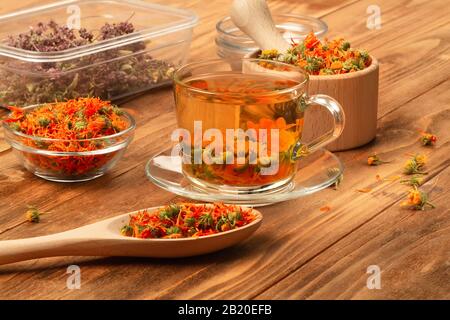 Mortier en bois avec fleurs thérapeutiques de calendula sèche, rosette avec calendula, tasse de thé avec fleurs de calendula sur une table en bois. Banque D'Images