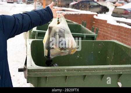 Yekaterinburg, Russie - Novembre 2019. La main d'un homme dans le déclencheur en hiver met le sac dans le conteneur à ordures.gros plan main tenant morceau de Banque D'Images