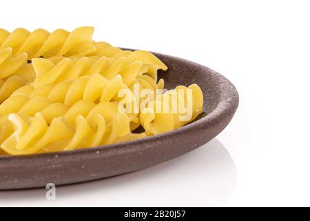 Beaucoup de fusilli de pâtes jaunes entières avec des dessous de verre en céramique brun isolé sur fond blanc Banque D'Images