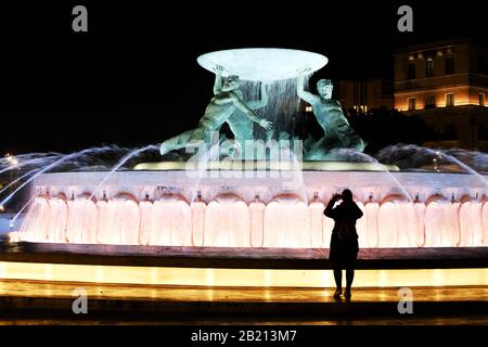 Jeune femme prenant une photo de fontaine éclairée avec trois tritons - site touristique de Valetta, Malte. Prise de vue nocturne Banque D'Images