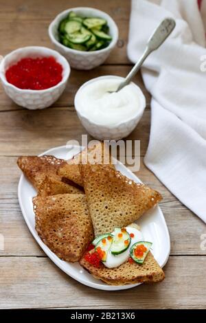 Crêpes au seigle et au grain entier servies avec de la crème sure, du caviar et des concombres. Style rustique. Banque D'Images