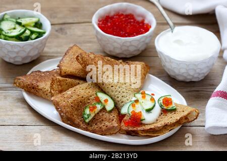 Crêpes au seigle et au grain entier servies avec de la crème sure, du caviar et des concombres. Style rustique. Banque D'Images