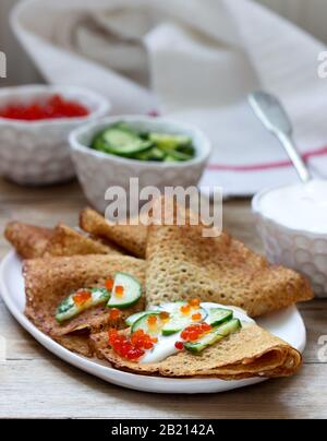 Crêpes au seigle et au grain entier servies avec de la crème sure, du caviar et des concombres. Style rustique. Banque D'Images