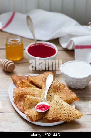 Crêpes au seigle et au grain entier servies avec de la crème aigre, du miel et de la sauce aux fraises. Style rustique. Banque D'Images
