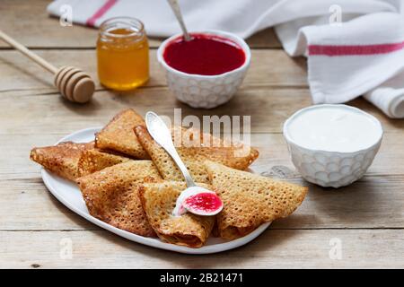Crêpes au seigle et au grain entier servies avec de la crème aigre, du miel et de la sauce aux fraises. Style rustique. Banque D'Images