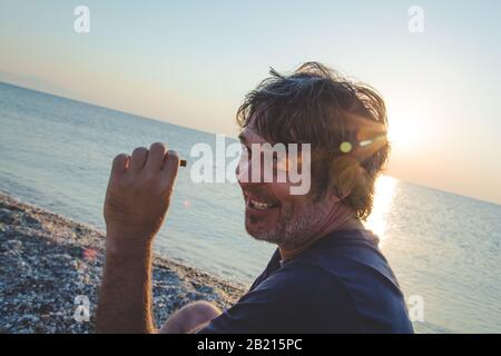 Charmant homme d'âge moyen avec un siège de cigare sur la plage tandis que couchers de soleil / gros portrait Banque D'Images