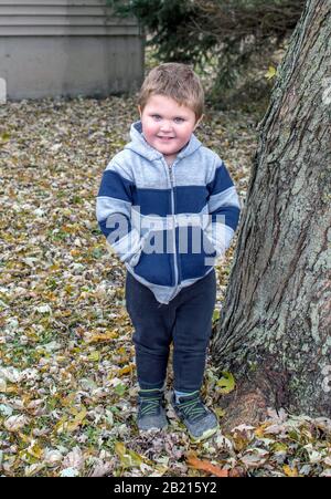 Un jeune garçon mignon se tient à l'extérieur avec les mains dans les poches de sa veste à capuche Banque D'Images