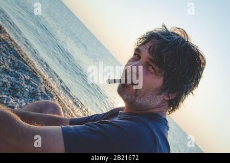 Charmant homme d'âge moyen avec un siège de cigare sur la plage tandis que couchers de soleil / gros portrait Banque D'Images