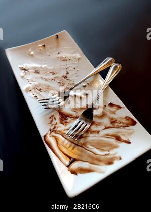 Une plaque en céramique fantaisie contient les restes d'un dessert au chocolat décadent avec deux fourchettes Banque D'Images