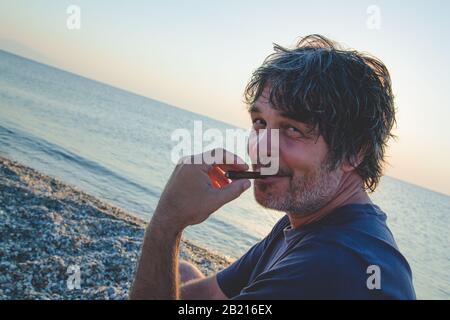 Charmant homme d'âge moyen avec un siège de cigare sur la plage tandis que couchers de soleil / gros portrait Banque D'Images