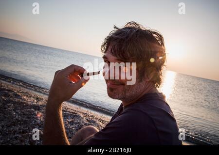 Charmant homme d'âge moyen avec un siège de cigare sur la plage tandis que couchers de soleil / gros portrait Banque D'Images