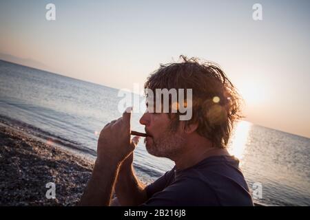 Charmant homme d'âge moyen avec un siège de cigare sur la plage tandis que couchers de soleil / gros portrait Banque D'Images