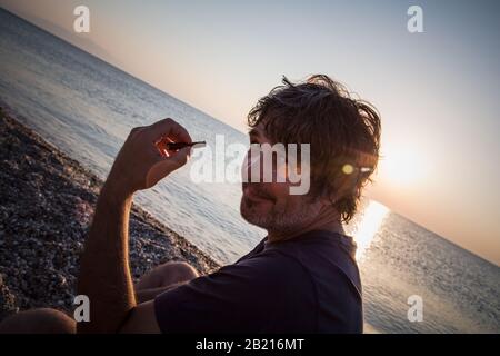 Charmant homme d'âge moyen avec un siège de cigare sur la plage tandis que couchers de soleil / gros portrait Banque D'Images