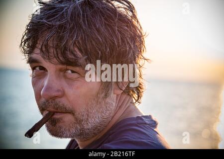 Charmant homme d'âge moyen avec un siège de cigare sur la plage tandis que couchers de soleil / gros portrait Banque D'Images