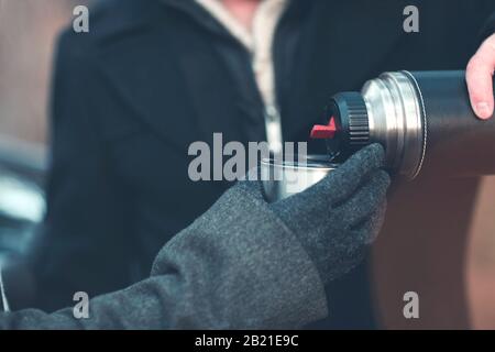 Croisez le coat et le gant chaud tenant la tasse en métal tandis que l'homme sans visage verser l'équipe chaude de thermos pendant la journée froide d'automne Banque D'Images