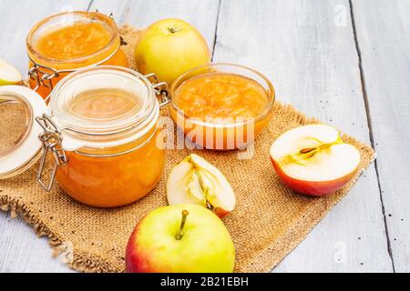 Confiture de pommes, confiture, chutney dans un pot en verre. Concept de préservation maison. Avec des pommes fraîches sur un sackCloth vintage, cuillère rustique sur planche en bois gris Banque D'Images