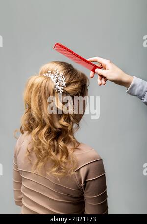Coupe des boucles d'ondes. Coiffeuse coiffeuse coiffante d'une femme blonde avec cheveux longs à l'aide d'un sabot sur fond gris. Coiffure professionnelle Banque D'Images