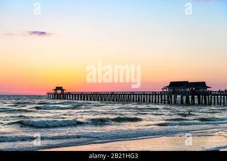 Naples, Floride coucher de soleil crépuscule dans le golfe du Mexique avec jetée en bois à l'horizon et silhouette vue sur les vagues de l'océan Banque D'Images