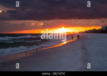 Coucher de soleil sombre coloré à Santa Rosa Beach avec la côte de Pensacola en Floride Panhandle au golfe du Mexique vagues de l'océan avec silhouette de personnes Banque D'Images