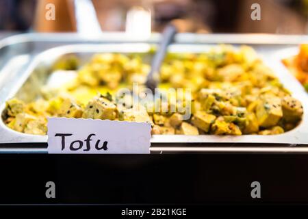 Des cubes de tofu cuits avec des légumes à l'épicerie du marché s'affichent à Florence, en Italie, avec un panneau sur le plateau buffet Banque D'Images