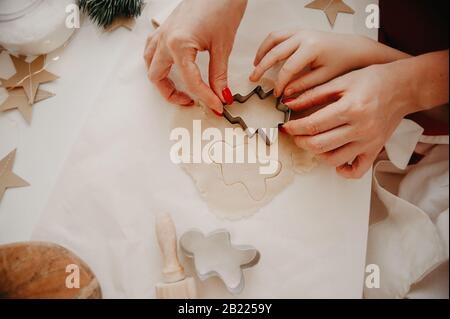les mains de maman et de bébé découpés les cookies de la pâte à l'aide de moules métalliques, sur du papier de cuisson, sur une table blanche avec décor à partir de stars du papier Banque D'Images