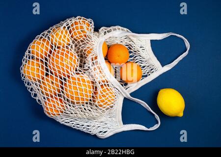 Sac de shopping en mesh avec tangerines, citrons sur fond bleu classique. Plat, vue du dessus. Zéro déchet, concept sans plastique. Une saine alimentation propre meurt Banque D'Images