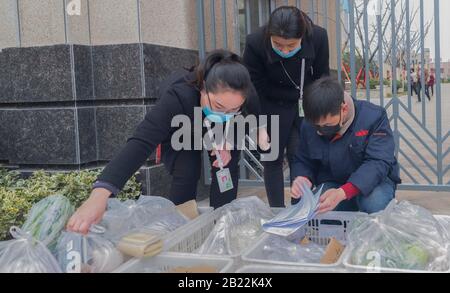 (200229) -- SANMENXIA, le 29 février 2020 (Xinhua) -- un membre du personnel d'une plateforme de commerce électronique et des travailleurs communautaires vérifie la réception de légumes commandés à la porte d'une communauté, à Sanmenxia, dans la province de Henan en Chine centrale, le 28 février 2020. Récemment, Sanmenxia a réalisé un projet visant à assurer l'approvisionnement en légumes pour les résidents par le biais d'un système de distribution communautaire développé par une plate-forme de commerce électronique. La plate-forme transporte les légumes des bases de plantation des agriculteurs locaux vers les communautés résidentielles. Les résidents locaux recueillent leurs commandes séparément. De cette façon, les résidents peuvent acheter des légumes frais Banque D'Images