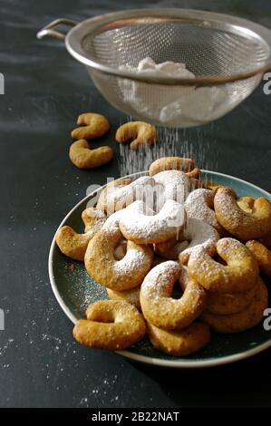 Biscuits aux noix fraîchement cuits avec du sucre en poudre qui les verse du tamiseur. Arrière-plan sombre flou et style rustique. Banque D'Images