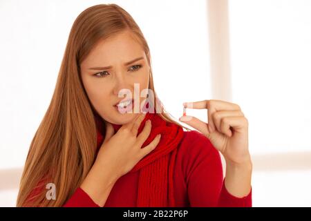 Jeune femme en pull rouge tient des pilules dans sa main comme elle est malade Banque D'Images