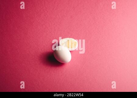 Oeuf blanc près de l'oeuf cuit pelé sur les couleurs rouges roses fond simple minimal, vue d'angle, heureux jour de Pâques Banque D'Images