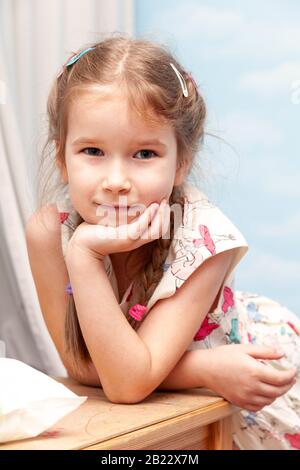 Petite jeune fille souriante souriante de l'école, se penchant sur une table avec la main sous son portrait de menton. Smug, expression smirk Banque D'Images