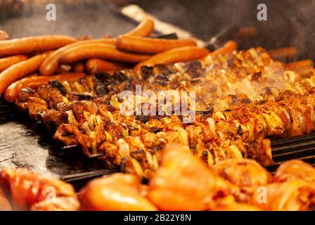 Il y a beaucoup de shashlik chaud et savoureux, des saucisses et de la viande sur barbecue extérieur. Cuisine différents types de viande, concept barbecue. Fumée au-dessus, photographie alimentaire Banque D'Images