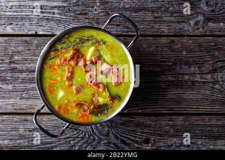 Soupe allemande aux pois fendus avec bacon, viande de porc, carotte, pomme de terre au thym - plat réconfortant d'hiver servi sur une casserole sur une ancienne table en bois de grange, vue sur le dessus, Banque D'Images