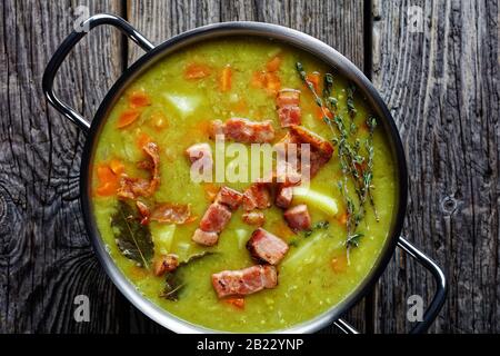 Soupe allemande de pois fendus erbseneintopf avec bacon, viande de porc, carotte, pomme de terre au thym - plat réconfortant d'hiver servi sur une casserole sur une ancienne grange W Banque D'Images