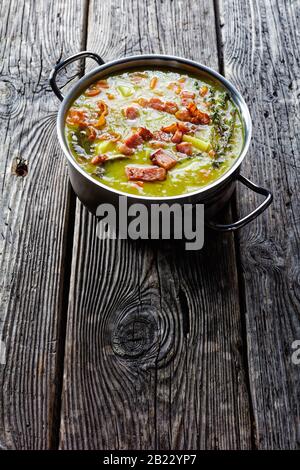 Soupe de pois en deux parties de la marcotte allemande avec bacon, viande de porc, carotte, pomme de terre au thym - plat réconfortant d'hiver servi sur une casserole sur une ancienne table en bois de grange, Banque D'Images