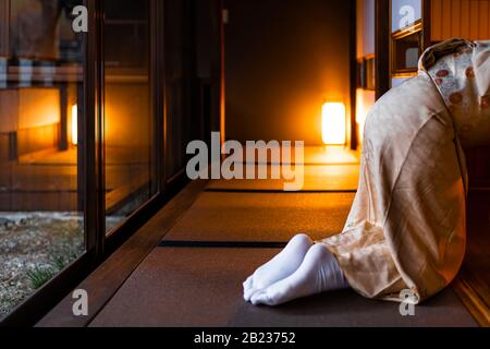 Maison traditionnelle japonaise de ryokan avec femme dans kimono et chaussettes de tabi ouvrant des portes coulissantes en papier de shoji assis sur le plancher de mat de tatami Banque D'Images