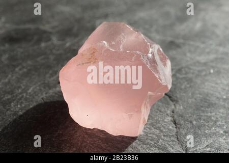 Caillou de quartz de rose non coupé et brut sur une tuile d'ardoise grise, éclairée par le soleil Banque D'Images