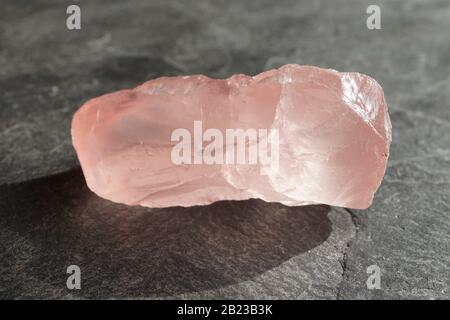 Caillou de quartz de rose non coupé et brut sur une tuile d'ardoise grise, éclairée par le soleil Banque D'Images