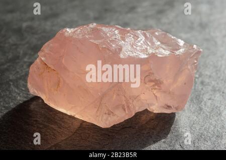 Caillou de quartz de rose non coupé et brut sur une tuile d'ardoise grise, éclairée par le soleil Banque D'Images