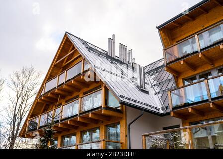 Une villa moderne en bois avec beaucoup de grandes fenêtres et un balcon avec un toit en étain recouvert de neige et de cheminées de ventilation en métal. Banque D'Images