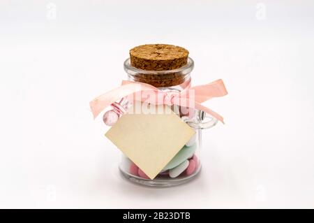 Amandes douces colorées dans un récipient en verre avec sucette et liège pour un baptême, sur fond blanc Banque D'Images