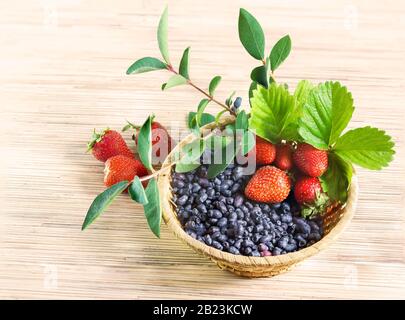 Baies de fraise mûre rouge, et miel bleu suckle Extrême-Orient dans un panier en osier avec des feuilles sur la table Banque D'Images