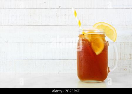 Thé glacé d'été dans un verre de pot de maçon. Vue latérale sur un fond en bois blanc. Banque D'Images