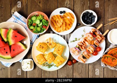 Barbecue d'été ou concept de pique-nique. Sélection de fruits, salade, viande grillée et pommes de terre. Vue sur le dessus de la scène de table sur un arrière-plan rustique en bois. Banque D'Images