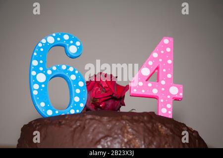 Numéros 64 sur un gâteau au chocolat. Bleu 6 et rose 4 signifiant 64 ans. Chocolat simple avec fleur rouge et 64 chiffres. Anniversaire. Banque D'Images