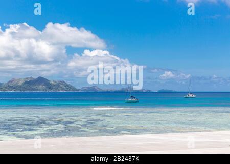 Yacht sur mer bleu turquoise, île de la Digue, île de Praslin à l'arrière, Seychelles, Océan Indien Banque D'Images