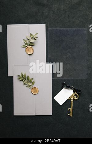 Invitation de mariage en plastique transparent sur fond gris. Il y a un joint sur l'enveloppe et une note sur la clé. Banque D'Images