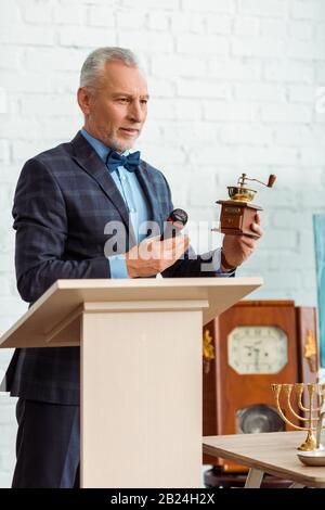 beau encanteur en costume pointant avec la main à la mouture de café et tenant le microphone pendant la vente aux enchères Banque D'Images