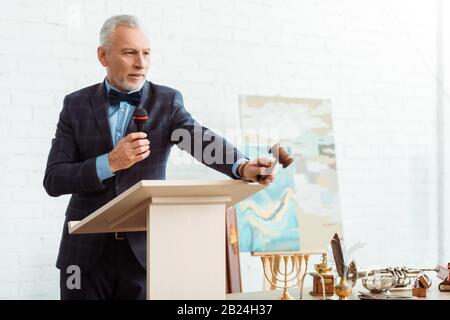 beau encanteur en costume parler avec le microphone et tenir le gavel pendant la vente aux enchères Banque D'Images