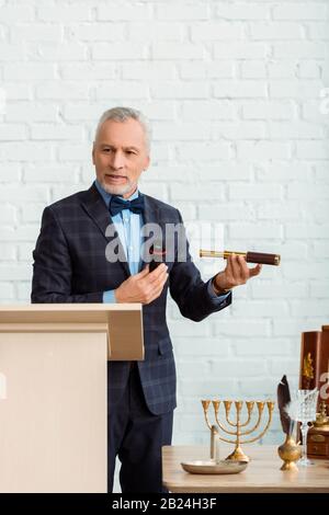 beau encanteur en costume parler avec le microphone et tenir le spyglass pendant la vente aux enchères Banque D'Images